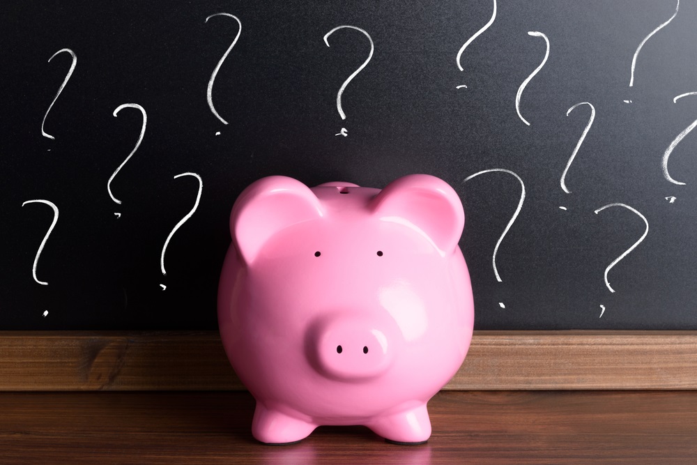 Pink piggy bank in front of a chalk board with question marks